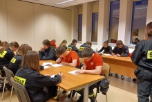 dzieci ubrane w mundury strażackie siedzą przy stołach i rozwiązuja test