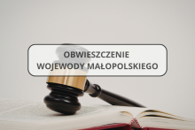 Na zdjęciu widoczna jest otwarta księga, na której spoczywa drewniany młotek sądowy. Na środku grafiki znajduje się jasny prostokąt w ozdobnej ramce, zawierający napis: Obwieszczenie Wojewody Małopolskiego