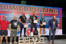 podoim trójboju siowego na nim zwycięzcy, obok po prawej mężczyzna w garniturze a po lewejs tronie dwóch mężczyzn w sporotwych ubraniach