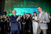 grupa ludzi ubrana w eleganckie stroje, z tyłu kolorowe światła