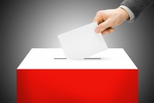 biało-czerwona urna, do której wkładany jest biały arkusz trzymany w dłoni