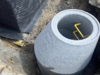 krąg betonowy w ziemi, w tle odkopany fundament budynku szkoły