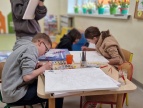 dzieci siedzą przy stole i malują farbami